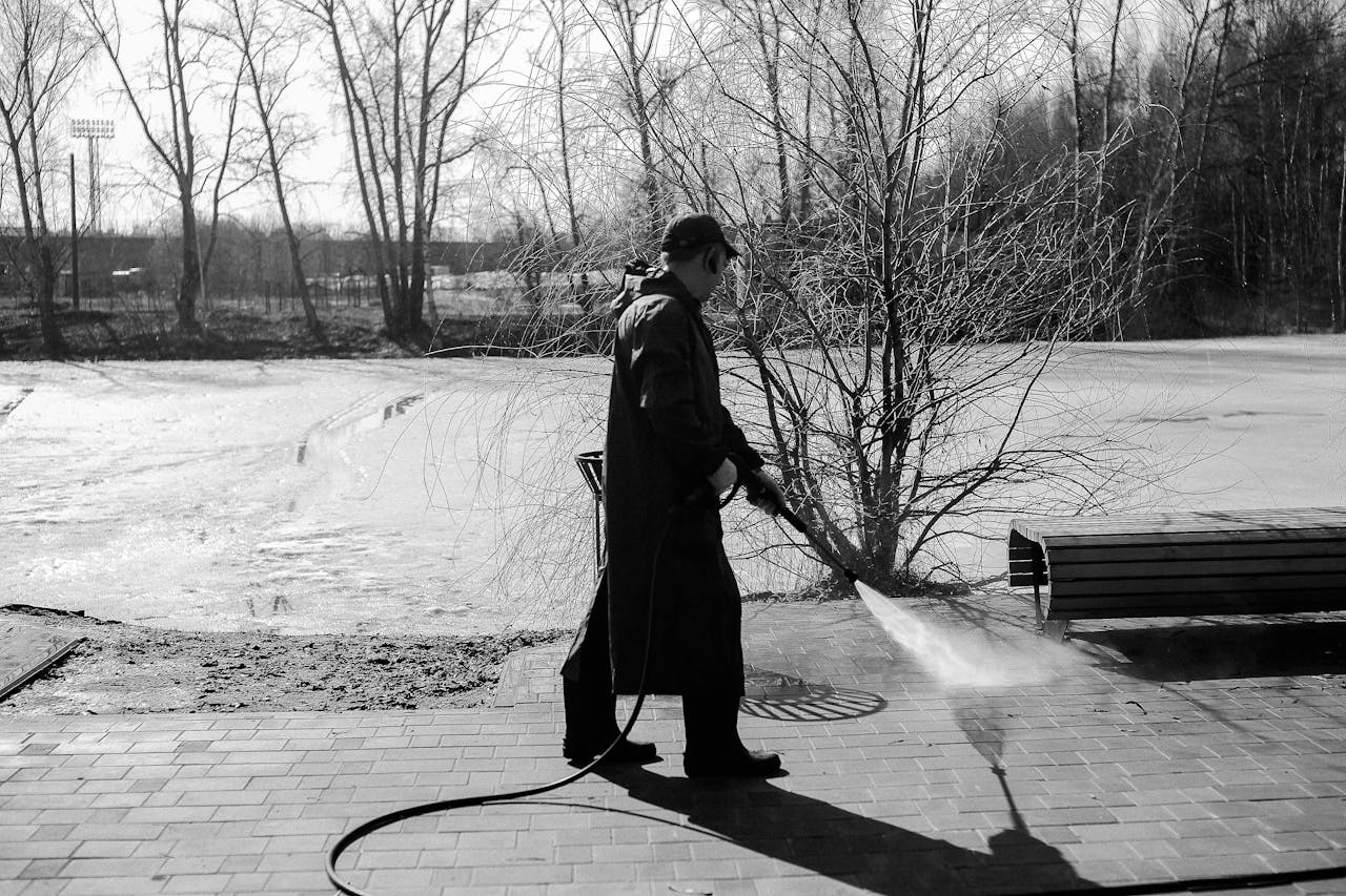 gallery-4 A man pressure washing pavement in a winter landscape captured in black and white.