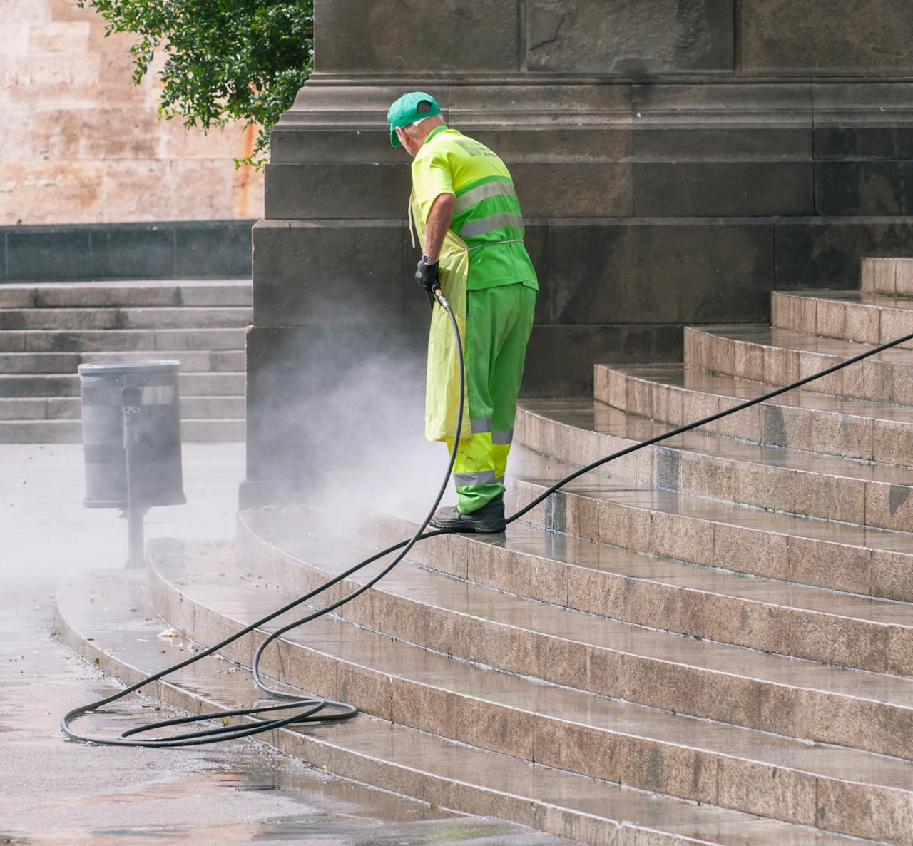 why-choose-us A street worker pressure washes stone stairs in a public park, ensuring cleanliness and safety.