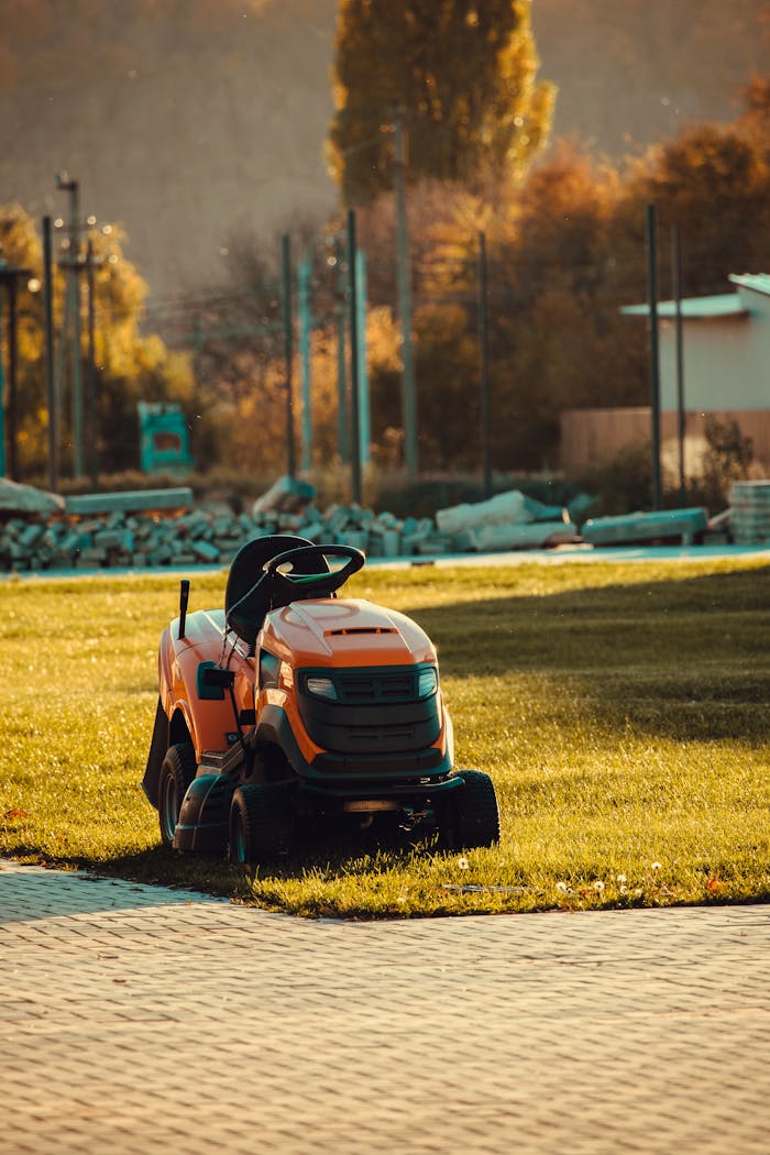 services-01 Vibrant orange lawn mower parked on a sunlit lawn during a beautiful autumn afternoon.