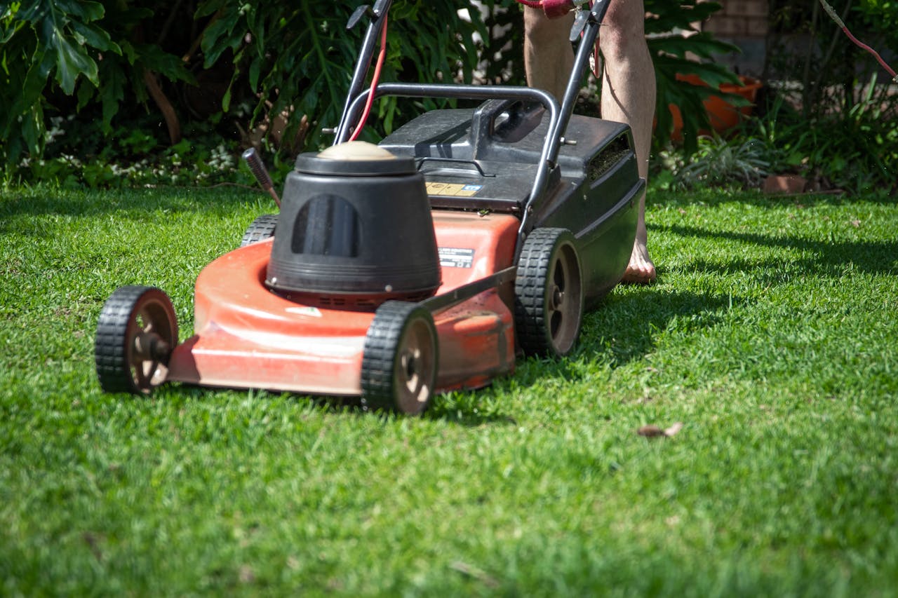 hero-img-02 A person operating a lawn mower on green grass, featuring gardening tools and lush foliage.