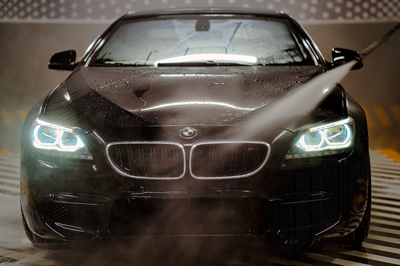 gallery-3 A sleek BMW being washed with water spray at night, highlighting the headlights and wet reflections.